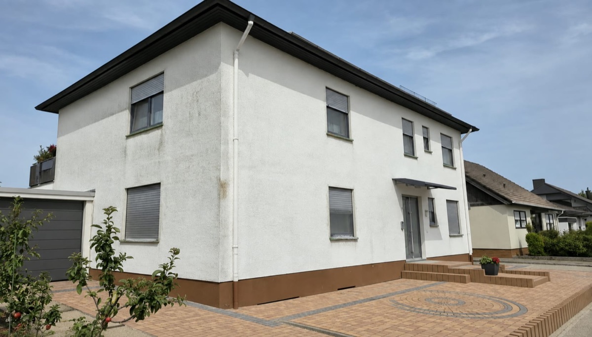 Zweigeschossiges Wohnhaus vor der Renovierung: verschmutzte weiße Fassade mit braunem Sockel